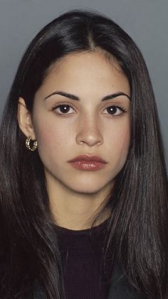 Woman with long dark hair and gold earrings looking directly at the camera