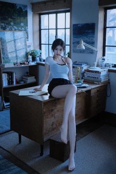 Woman in a white t-shirt and black shorts sitting on a desk indoors