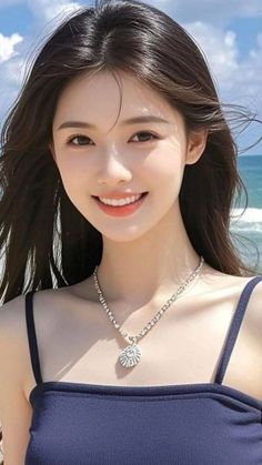 Woman with long dark hair and a necklace smiling at the beach