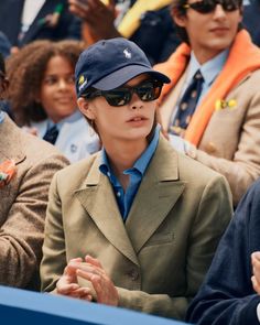 Woman in a baseball cap and sunglasses watching an event outdoors