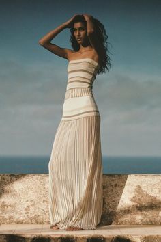 Woman in a striped strapless dress with a pleated skirt overlooking the ocean