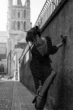 Woman in a polka dot dress adjusting her shoe on a cobblestone street