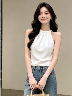 Woman with long dark hair wearing a white halter top and blue jeans, holding a straw bag