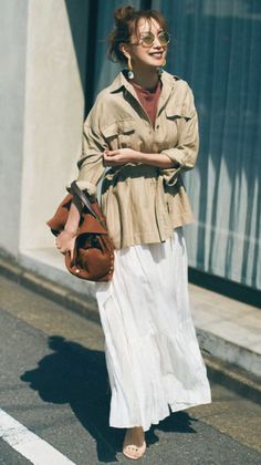 Woman in a khaki shirt and white skirt with a brown bag and sunglasses outdoors