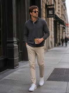 Man in a dark gray shirt and khaki pants walking on a city street with a coffee cup