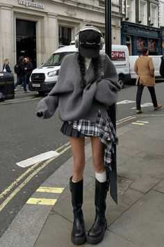 Person in a plaid skirt, oversized sweater, and knee-high boots on a city street