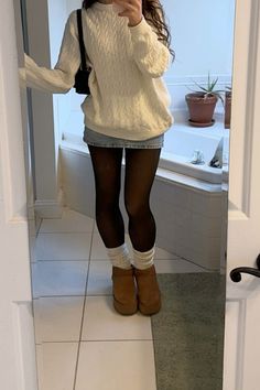 Person in a cable knit sweater, denim skirt, and black tights taking a mirror selfie