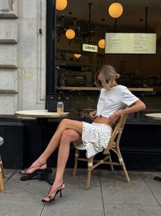 Woman in a polka dot skirt and knotted t-shirt sitting at an outdoor cafe