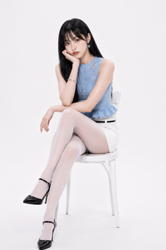 Woman with long black hair wearing a blue top and white shorts, sitting on a chair