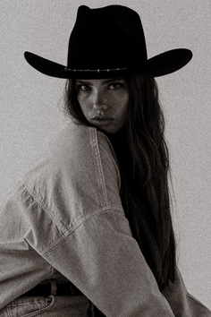 Woman in a cowboy hat and denim jacket looking over her shoulder
