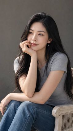 Woman with long black hair wearing a grey t-shirt and blue jeans, looking away