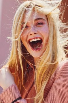 Blonde woman with freckles and pink makeup, laughing with windblown hair