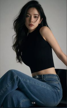Woman with long black hair wearing a black crop top and blue jeans in a studio