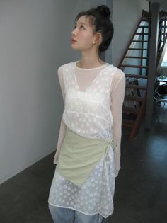 Woman in a white sheer top and light green wrap skirt looking up indoors