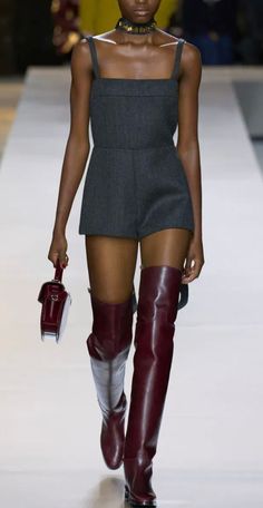 Woman with dark skin in a gray romper and red thigh-high boots on a runway