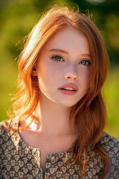 Close-up portrait of a young woman with red hair and blue eyes outdoors