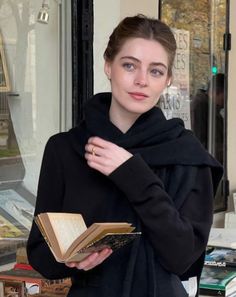 Woman with blue eyes and a black scarf holding a book outdoors