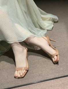 Woman's feet in nude high heels under a sheer, sparkly dress