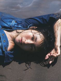 Woman in a denim jumpsuit lying on dark wet sand at the beach