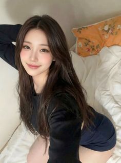 Woman with long dark hair in a black shirt posing on a bed