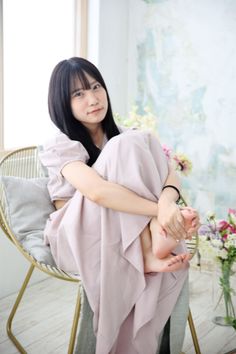 Woman with long black hair in a light pink dress sitting indoors