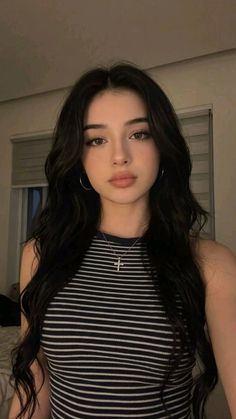 Woman with long wavy hair wearing a striped top and cross necklace indoors