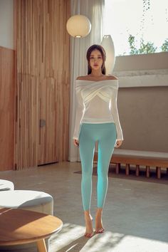 Woman in an off-shoulder top and blue leggings posing indoors