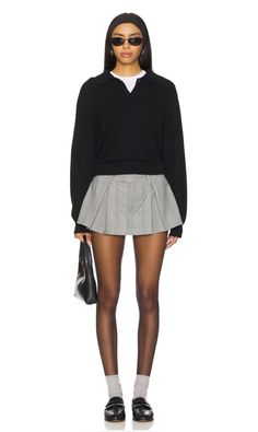 Woman in a black sweater and pleated skirt with sunglasses and a handbag