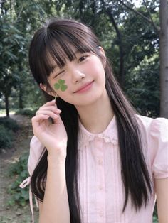 Young woman with long dark hair holding a clover and winking outdoors