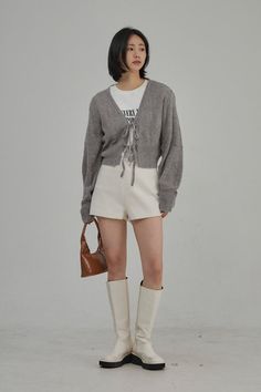 Woman in a gray cardigan, white shorts, and knee-high boots holding a brown handbag