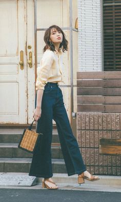 Woman in a yellow shirt and wide leg jeans holding a wicker bag outdoors