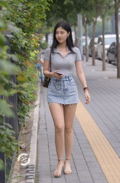 Woman in a grey polo shirt and denim skirt walking on a street