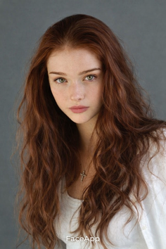 Woman with long red hair and green eyes wearing a white shirt and cross necklace
