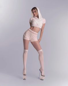 Woman in a crop top hoodie, shorts, and thigh-high socks posing in a studio