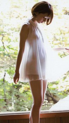 Woman in a sheer white dress standing by a window with backlight
