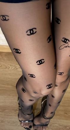Legs in black tights with Chanel logos and high heels on a wooden floor