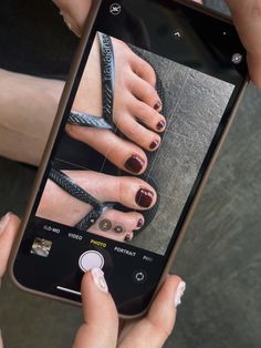 Person holding a phone taking a photo of feet in flip flops with dark red nail polish