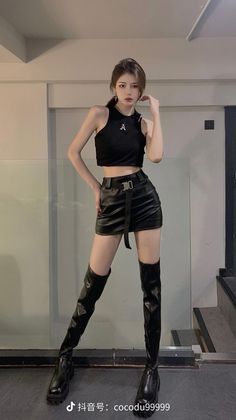 Woman in a black crop top, leather mini skirt, and thigh high boots indoors