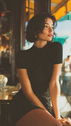 Woman with short hair in a black dress sitting by a window with soft lighting
