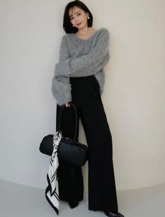 Woman in a gray fuzzy sweater and black pants holding a black handbag