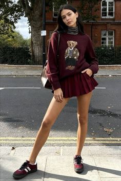 Woman in a burgundy sweater and pleated skirt standing on a street