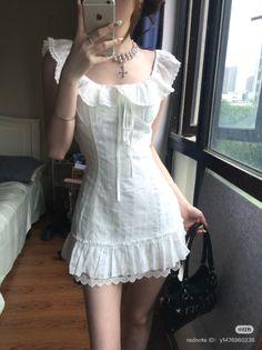 Woman in a white ruffle dress and pearl necklace taking a mirror selfie