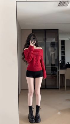 Woman in a red off-shoulder sweater and black shorts taking a mirror selfie