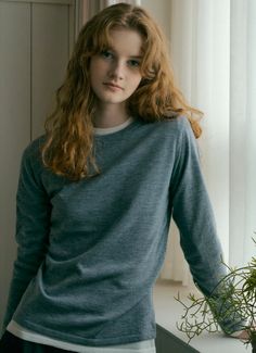 Young woman with long wavy hair wearing a blue shirt indoors by a window