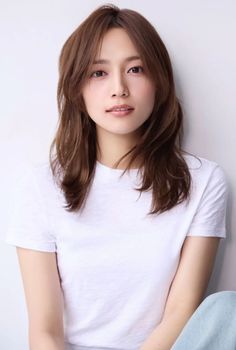 Woman with long brown hair wearing a white t-shirt against a light background
