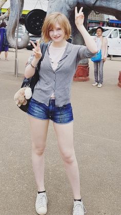 Woman with short hair in denim shorts and a cardigan posing outdoors