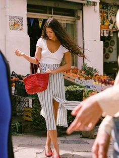Woman with long hair holding a red bag at an outdoor fruit stand