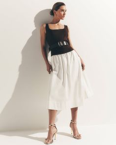 Woman in a brown top and white skirt with a belt and high heels