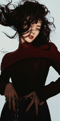 Woman with long dark hair and red lipstick wearing dark clothing and jewelry