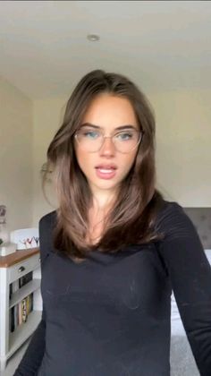 Woman with long brown hair and glasses wearing a black shirt indoors